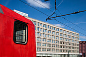 Ein leuchtend roter DB Regio-Zug fährt in den Bahnhof Alexanderplatz ein, umgeben von den architektonischen Sehenswürdigkeiten Berlins unter einem strahlend blauen Himmel