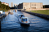 A boat glides along the Spree River by Schlossplatz, surrounded by green spaces and historical architecture in Berlin.