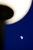 A streetlamp is illuminated while the crescent moon glows in the dark blue sky, creating a tranquil nighttime atmosphere.