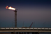 A flaring tower operates at a regasification facility along the coast of Huelva, showcasing energy activities in southwestern Spain.