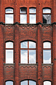 The striking red brick facade in Mitte, Berlin, features large windows reflecting the sky and demonstrating rich architectural heritage.