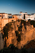 Charming whitewashed houses rise above El Tajo gorge, showcasing Rondas picturesque beauty during a serene sunset.