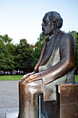 The statue of Karl Marx sits prominently in the Marx-Engels-Forum, surrounded by lush green parks in Berlin\'s Mitte district.