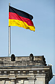 The German flag waves above the Reichstag building, a key landmark in Berlin, representing the country\'s political history.