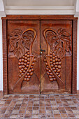 Hand-carved wooden doors with bas relief grape clusters at the entrance of the Portal del Santo Hotel in Cafayate, Argentina.