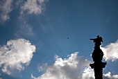 The statue of Columbus stands tall, pointing decisively towards the horizon amidst a backdrop of clouds in Barcelona.