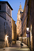 Visitors stroll down Calle de la Compañía, admiring historic architecture as the University Pontifica and Clerecía towers light up dusk.