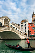 Gondolier dressed in traditional white and red paddling a gondola boat with tourists on the Grand Canal underthe  Rialto Bridge, Venice, UNESCO World Heritage Site, Veneto, Italy, Europe