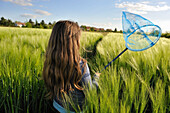 Little girl with a butterfly net in  field of  barley, Commune de Senantes, Departement d'Eure-et-Loir, Centre, France, Europe