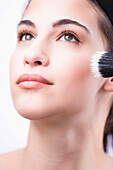 Close up of a young woman applying make with a blush brush