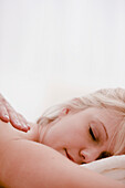 Close up of a woman face resting on a white towel with a man hand massaging her shoulder