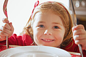 Smiling Girl at Dining Table Holding Knife and Fork