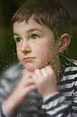 Boy with Hands on Chin behind Rainy Window