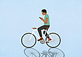 Man with smart phone texting and riding bicycle on blue background