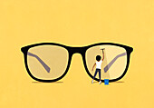 Woman with squeegee cleaning lens of large eyeglasses on yellow background