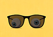 Eyeballs behind large, tinted sunglasses on yellow background