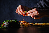 Woman topping rib tacos at a dark table