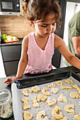 Young girl and adult baking biscuits in a modern kitchen