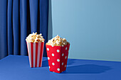 Two popcorn containers on a blue table and background