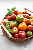 A colourful mix of fresh tomatoes in a woven basket on a ki