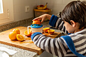 Little boy makes fresh orange juice in a cosy kitchen