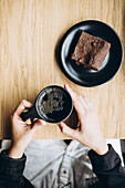 Hands holding coffee cup and brownie on plate