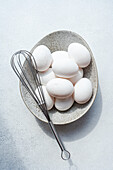 Top view of fresh raw chicken eggs in a bowl with whisk