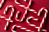 Top view of scattered candy canes on red background