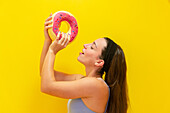 Woman holding a colourful doughnut against a yellow background