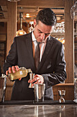 Bartender pouring alcohol into a measuring cup while preparing a cocktail