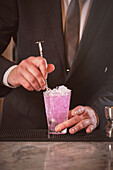 Barkeeper im schwarzen Anzug mixt Cocktail am Tresen