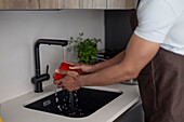 Close-up of a man washing a red pepper under running water