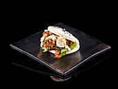 Asiatisches Gourmet Bao Brötchen mit frischen Zutaten auf schwarzem Teller