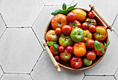 A colourful selection of tomatoes in a woven basket on a textured floor
