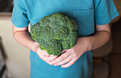 Anonymous child holds a large broccoli in his hands