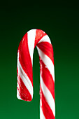 Close-up of a red and white candy cane against a green background