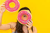 Playful woman with doughnut eyes on a yellow background
