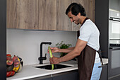 Man washes a long green vegetable under running water in a factory