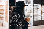 Stylish woman with pigtails uses her smartphone in a shop