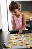 Young girl decorating biscuits on a baking tray