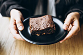 Close-up of hands holding a chocolate brownie on a plate
