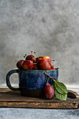 Fresh organic plums in a ceramic cup on a wooden background