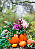 Herbstliches Arrangement mit Kürbisvase, Gemüsekohl (Brassica oleracea), Efeu (Hedera helix), Dahlien (Dahlia) auf Holztisch