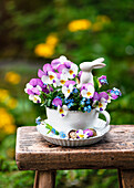 Frühlingsstrauß aus Garten-Stiefmütterchen (Viola wittrockiana) und Vergissmeinnicht (Myosotis) in Tasse, Osterhase