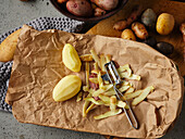 Raw, peeled potatoes and potato peelings on a paper bag