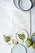 Fresh artichokes, plate with artichoke motif and several tart moulds