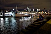 Vereinigtes Königreich, London, Southwark, Liebespaar am Ufer der Themse am Bankside Pier, im Hintergrund die Wolkenkratzer der City