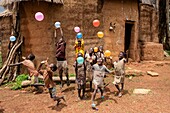 Benin, Nothern distict, Atacora mountains area, Koussoukoingou, children playing with ballons in front of a Tata made with banco (soil mixed with straw), traditional defensive two-storey habitat typical of northern Benin