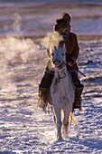 China, Innere Mongolei, Provinz Hebei, Zhangjiakou, Bashang-Grasland, ein mongolischer Reiter auf einem Pferd, der auf einer schneebedeckten Wiese läuft