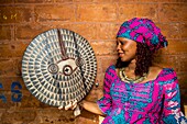 Benin, Cotonou, woman wearing traditional clothes holding handcraft object at the craft market